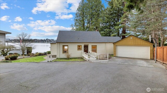 view of front facade with an outbuilding, fence, roof with shingles, a garage, and a water view