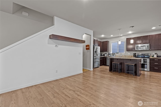 kitchen with light wood finished floors, dark brown cabinetry, a breakfast bar area, light countertops, and appliances with stainless steel finishes