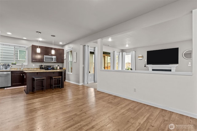 kitchen featuring a kitchen bar, open floor plan, stainless steel appliances, light wood-style floors, and dark brown cabinetry