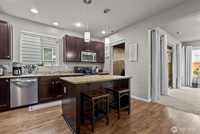 kitchen featuring light stone counters, a kitchen breakfast bar, stainless steel appliances, dark brown cabinetry, and light wood-style floors