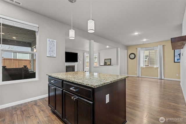 kitchen with wood finished floors, baseboards, a fireplace, hanging light fixtures, and open floor plan