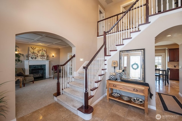 stairway featuring a premium fireplace, baseboards, arched walkways, and a towering ceiling