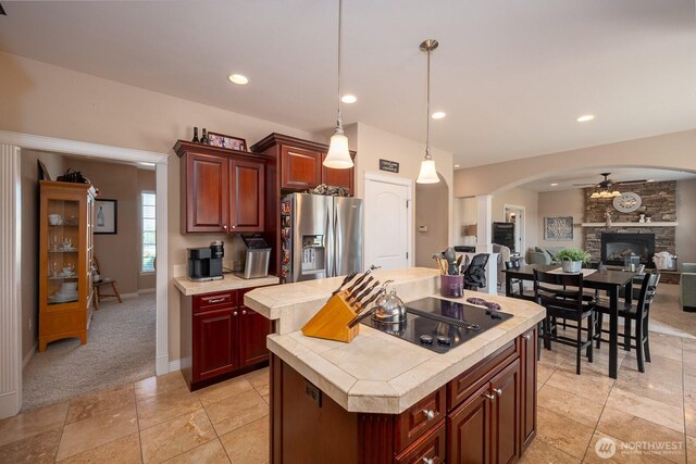 kitchen featuring a ceiling fan, a center island, stainless steel fridge, arched walkways, and black electric cooktop