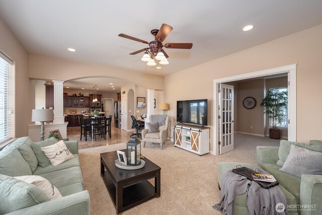 living area featuring decorative columns, recessed lighting, arched walkways, ceiling fan, and light carpet