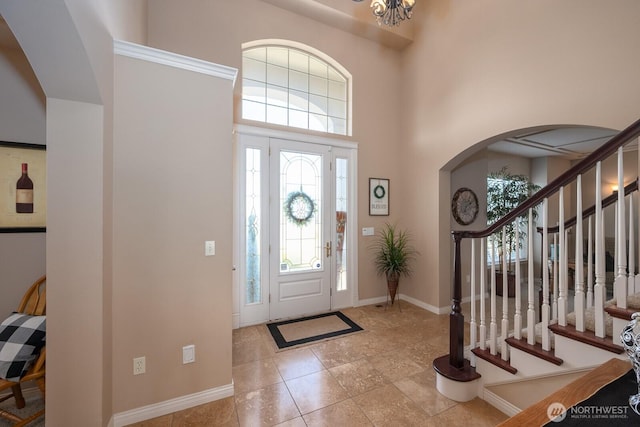 foyer with stairway, baseboards, an inviting chandelier, arched walkways, and a towering ceiling