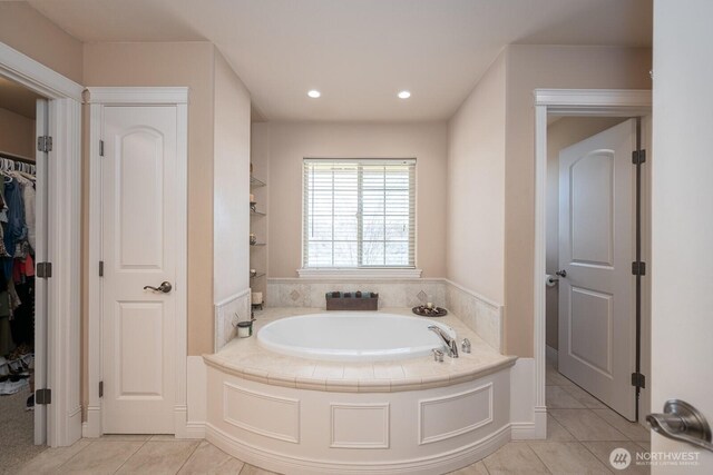 bathroom with a walk in closet, a garden tub, recessed lighting, and tile patterned floors