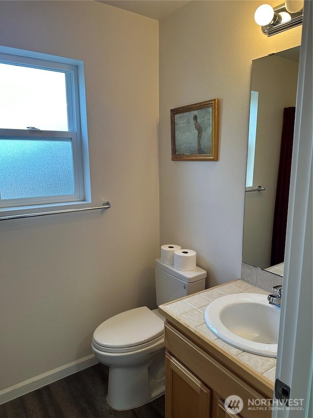 half bathroom with baseboards, vanity, toilet, and wood finished floors