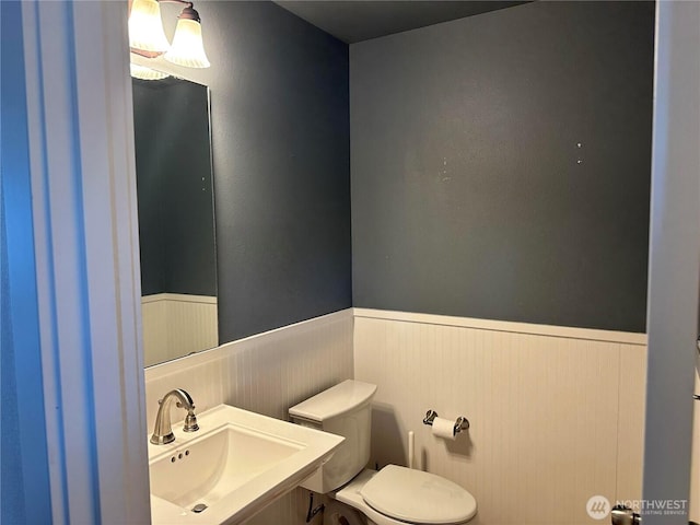 half bath featuring toilet, a wainscoted wall, and a sink