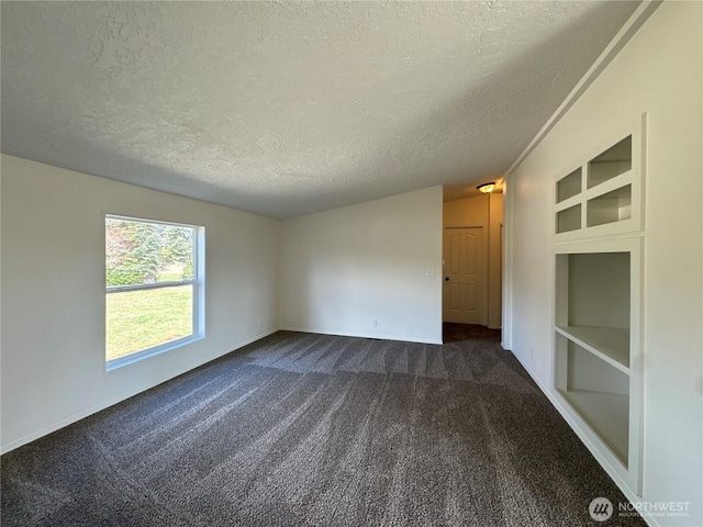 spare room featuring a textured ceiling, built in shelves, dark carpet, and baseboards