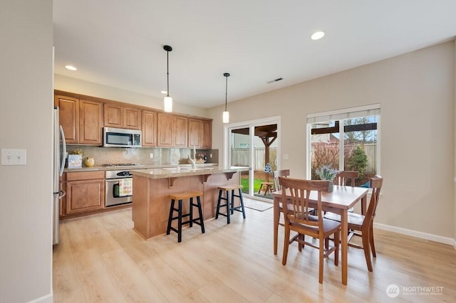 kitchen featuring light wood-style flooring, tasteful backsplash, stainless steel appliances, a breakfast bar area, and brown cabinetry