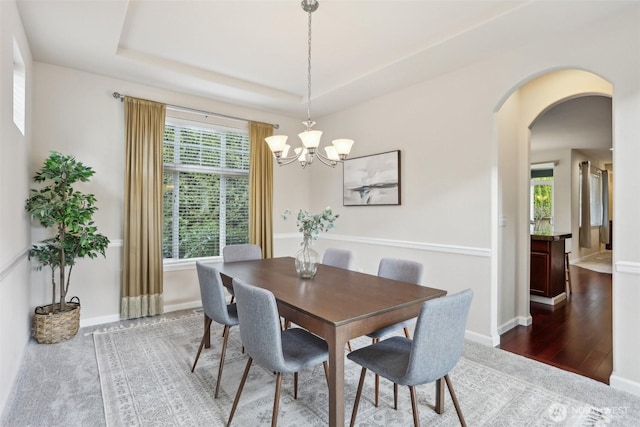 dining room featuring arched walkways, a chandelier, a raised ceiling, and baseboards