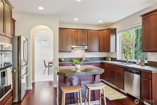 kitchen with appliances with stainless steel finishes, a kitchen bar, a kitchen island, recessed lighting, and arched walkways
