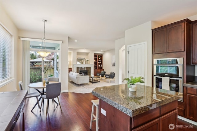 kitchen featuring stainless steel double oven, dark wood finished floors, a glass covered fireplace, a center island, and a kitchen bar