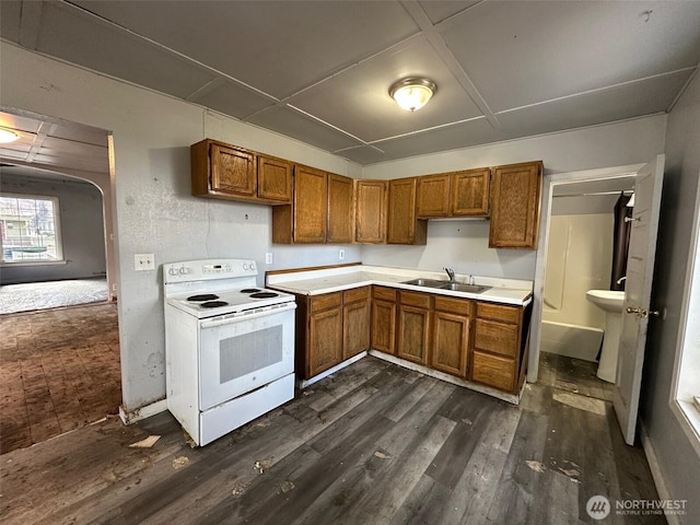 kitchen with white electric range oven, dark wood-style floors, brown cabinets, light countertops, and a sink