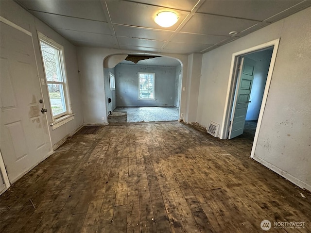 corridor featuring arched walkways, wood-type flooring, and plenty of natural light