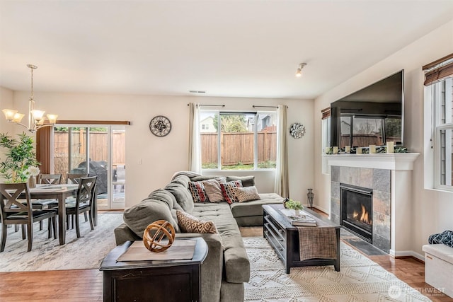 living area featuring light wood-type flooring, visible vents, a fireplace, baseboards, and a chandelier