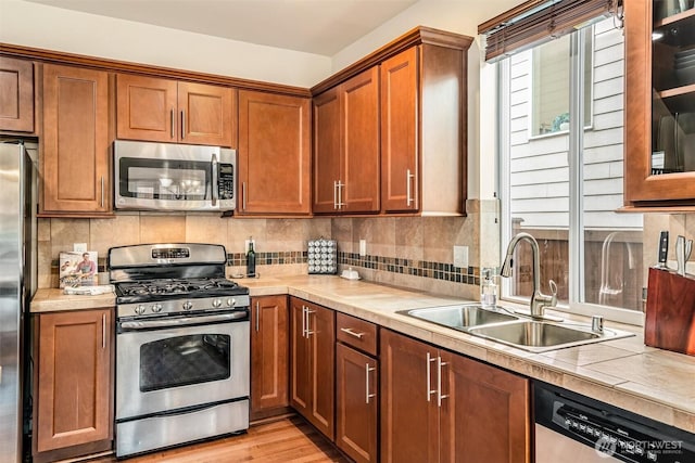 kitchen with light wood-type flooring, a sink, appliances with stainless steel finishes, tasteful backsplash, and brown cabinets