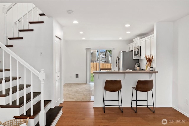 kitchen with wood finished floors, a breakfast bar, recessed lighting, appliances with stainless steel finishes, and white cabinetry