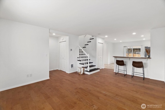 unfurnished living room with stairway, wood finished floors, visible vents, baseboards, and recessed lighting