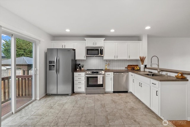 kitchen with dark countertops, decorative backsplash, appliances with stainless steel finishes, a peninsula, and a sink