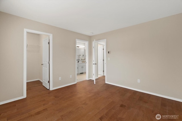 unfurnished bedroom featuring a spacious closet, baseboards, and wood finished floors