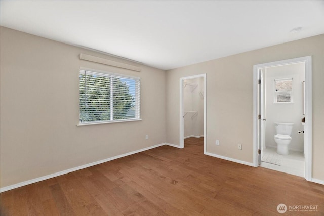 unfurnished bedroom featuring a spacious closet, baseboards, ensuite bathroom, wood finished floors, and a closet