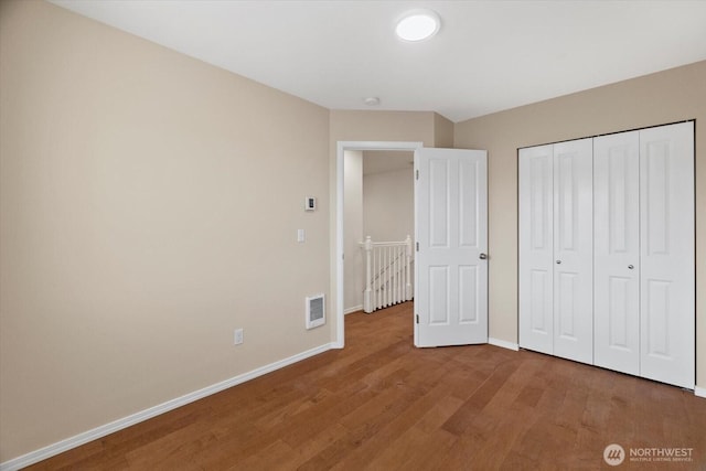 unfurnished bedroom with a closet, baseboards, visible vents, and wood finished floors