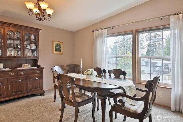 dining area with light carpet, a chandelier, plenty of natural light, and vaulted ceiling