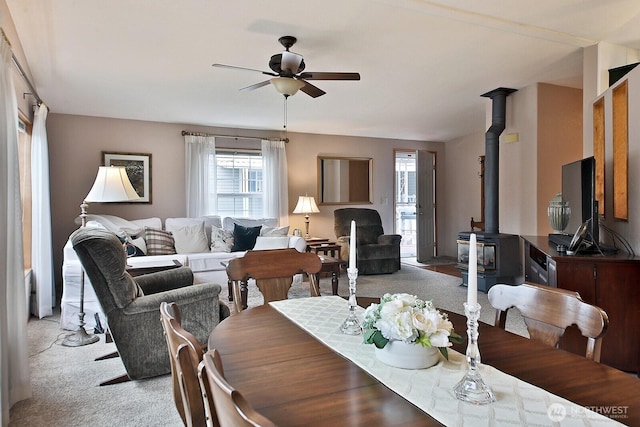 dining space featuring a ceiling fan, a wood stove, and light colored carpet