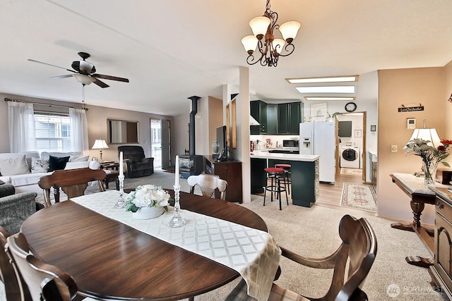 dining area with washer / dryer, a wood stove, ceiling fan with notable chandelier, and light wood-style floors