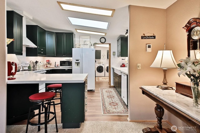 kitchen featuring white appliances, a peninsula, a skylight, light countertops, and independent washer and dryer