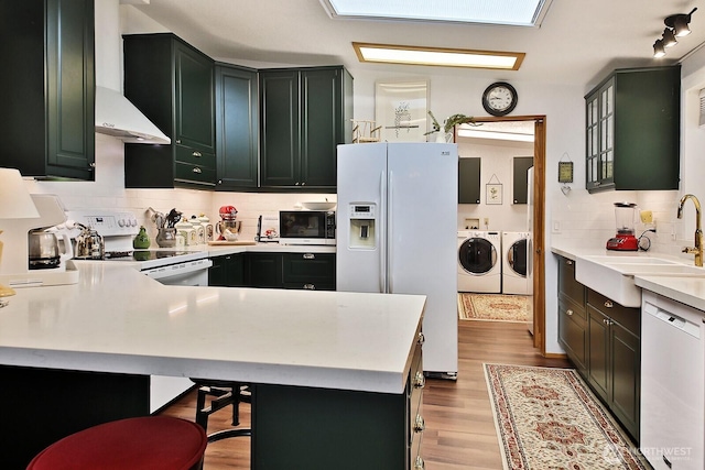 kitchen featuring light wood-style flooring, washer and clothes dryer, a sink, white appliances, and light countertops