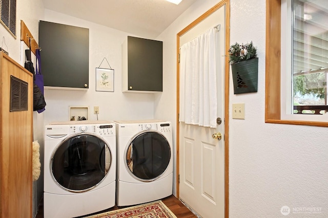 laundry area featuring washer and clothes dryer, visible vents, cabinet space, and wood finished floors