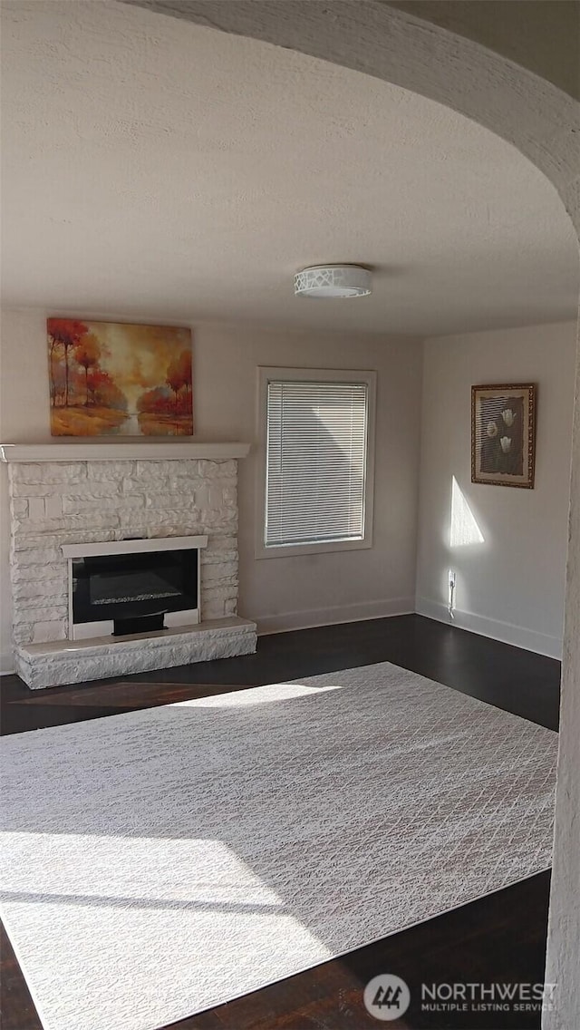 unfurnished living room featuring dark wood finished floors, a stone fireplace, a textured ceiling, and baseboards