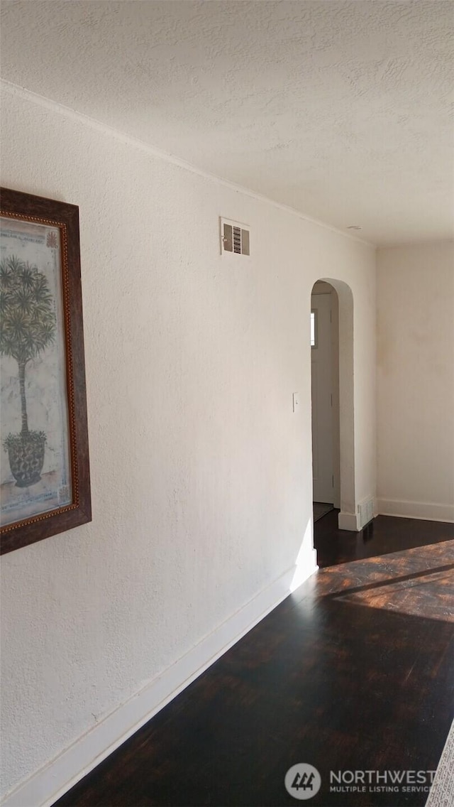 empty room featuring visible vents, baseboards, arched walkways, a textured ceiling, and a textured wall