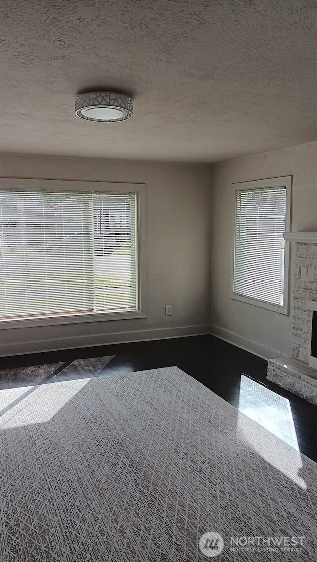 empty room with a fireplace, a textured ceiling, and baseboards