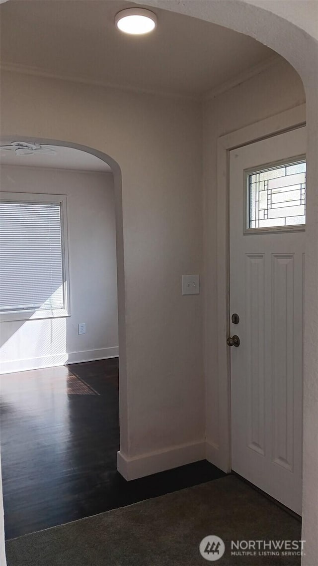 foyer with dark wood finished floors, crown molding, baseboards, and arched walkways