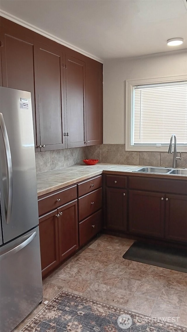 kitchen with a sink, tasteful backsplash, freestanding refrigerator, dark brown cabinetry, and light countertops