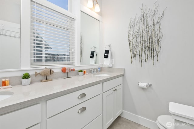 bathroom featuring baseboards, a sink, toilet, and double vanity