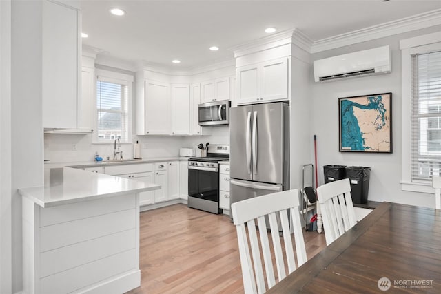 kitchen with light wood finished floors, a wall unit AC, appliances with stainless steel finishes, white cabinetry, and a sink