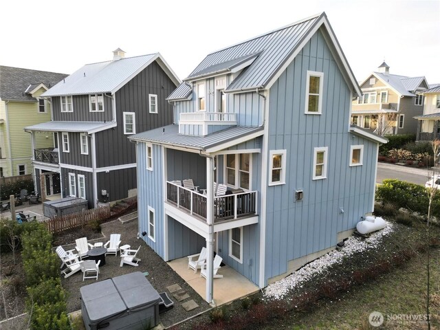 back of house with board and batten siding, a standing seam roof, a patio area, and a balcony