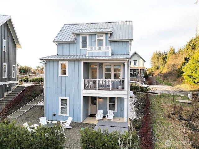 back of house with metal roof, a balcony, stairway, board and batten siding, and a standing seam roof