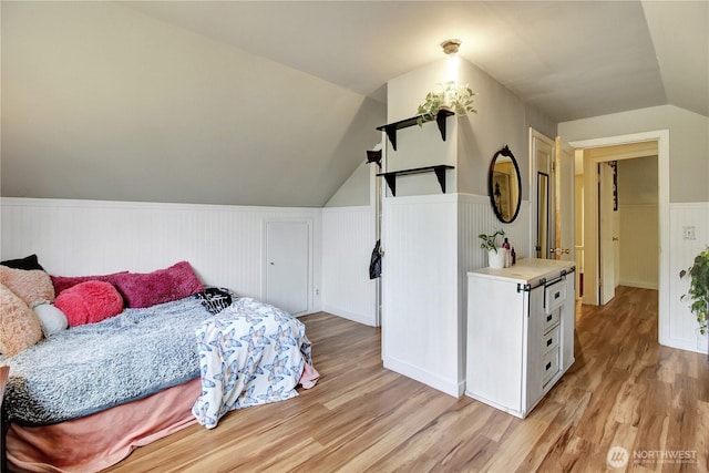 bedroom featuring lofted ceiling, wainscoting, and light wood finished floors