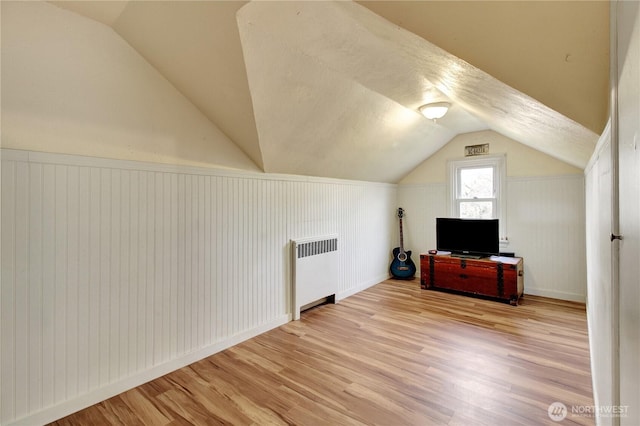 bonus room featuring vaulted ceiling, radiator, and wood finished floors