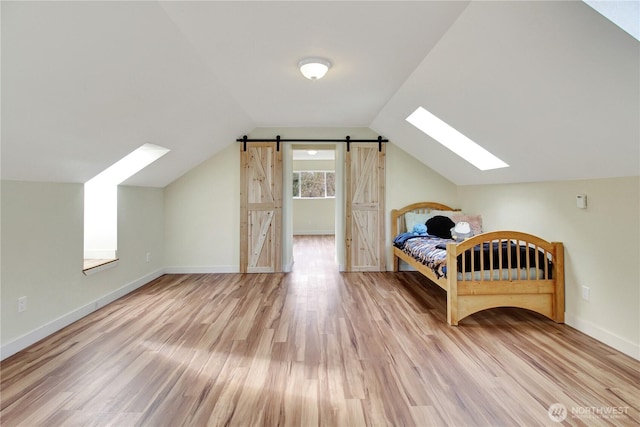 unfurnished bedroom featuring a barn door, vaulted ceiling with skylight, wood finished floors, and baseboards