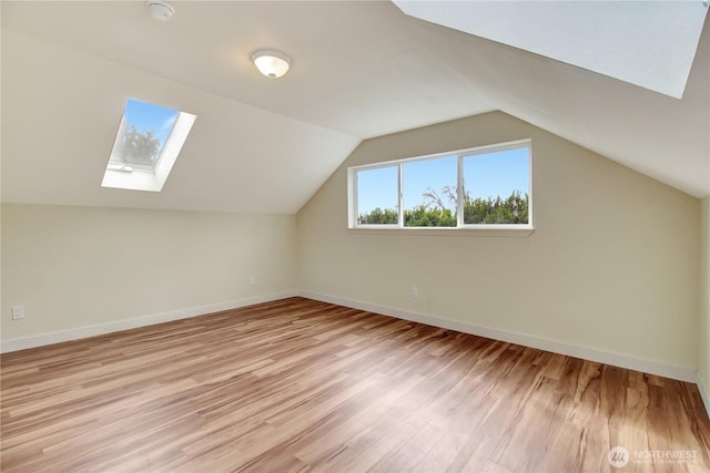 additional living space with lofted ceiling with skylight, light wood-style flooring, and baseboards