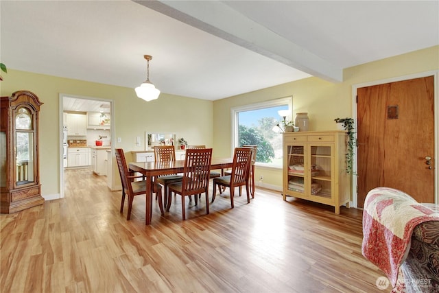 dining area featuring beam ceiling, baseboards, and light wood-type flooring