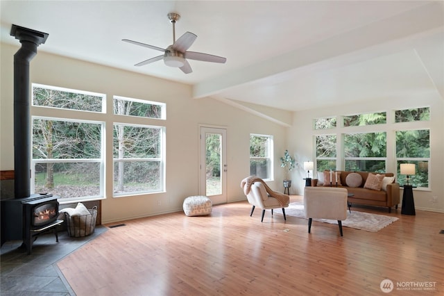 interior space with a ceiling fan, wood finished floors, baseboards, lofted ceiling with beams, and a wood stove