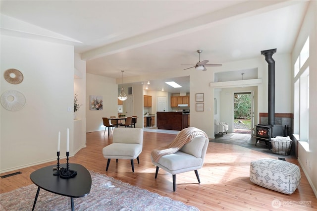 sitting room with light wood finished floors, visible vents, a wood stove, and baseboards