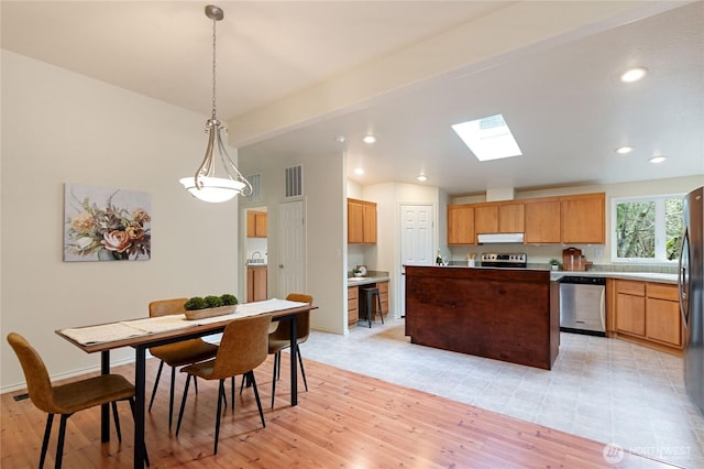 kitchen featuring light wood finished floors, visible vents, a center island, lofted ceiling with skylight, and stainless steel appliances